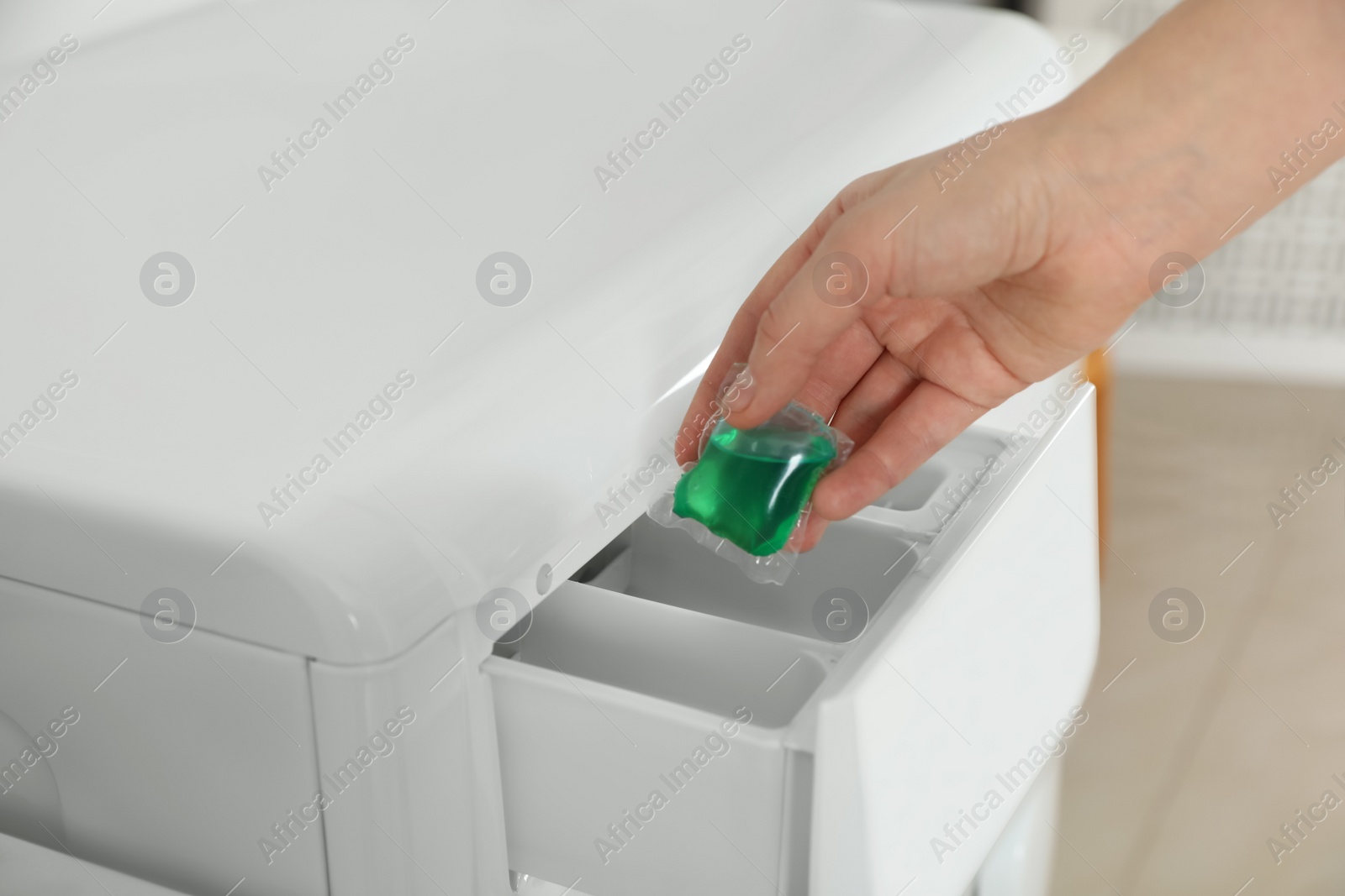 Photo of Woman putting laundry detergent capsule into washing machine, closeup