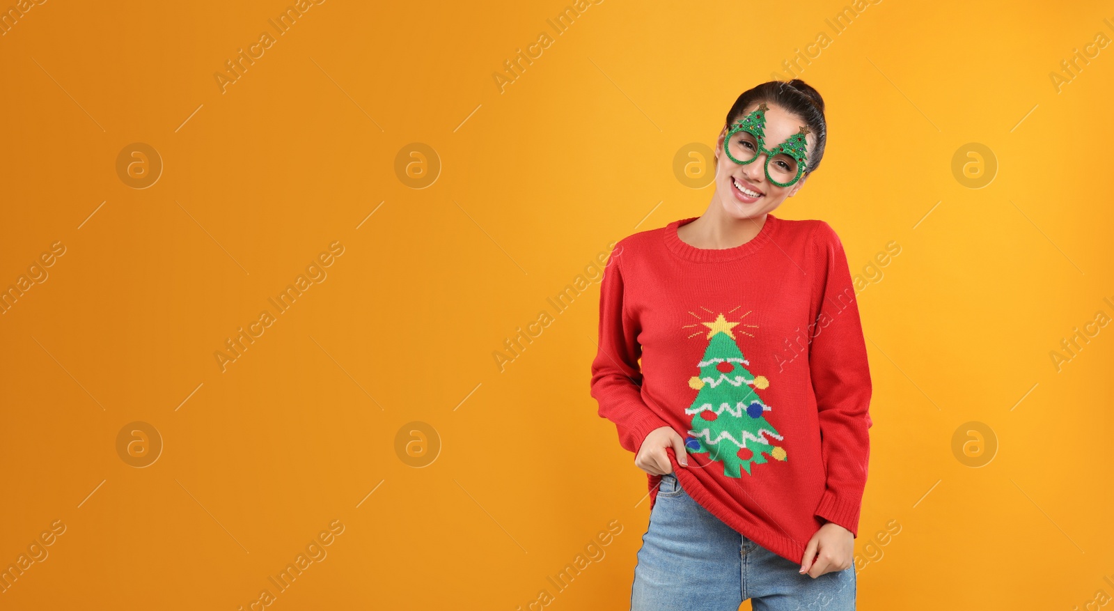 Photo of Young woman in Christmas sweater and party glasses on yellow background, space for text