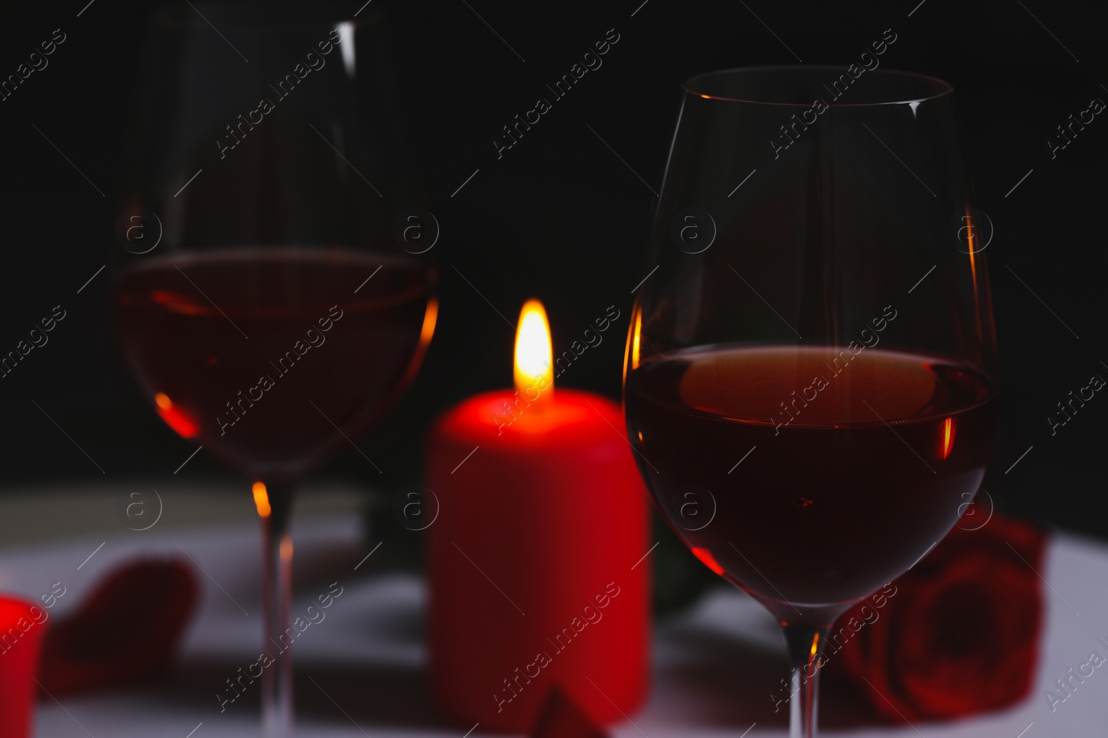 Photo of Glasses of red wine, rose flower and burning candle on table. Romantic atmosphere