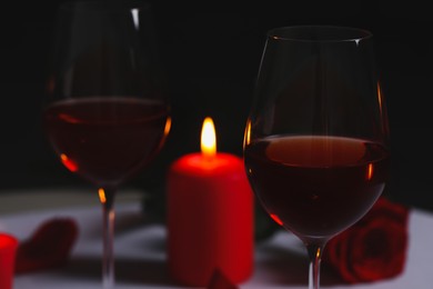 Photo of Glasses of red wine, rose flower and burning candle on table. Romantic atmosphere