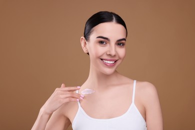 Photo of Beautiful woman with smear of body cream on her collarbone against light brown background