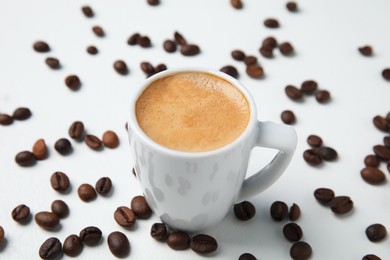 Photo of Cup of tasty espresso and scattered coffee beans on white table