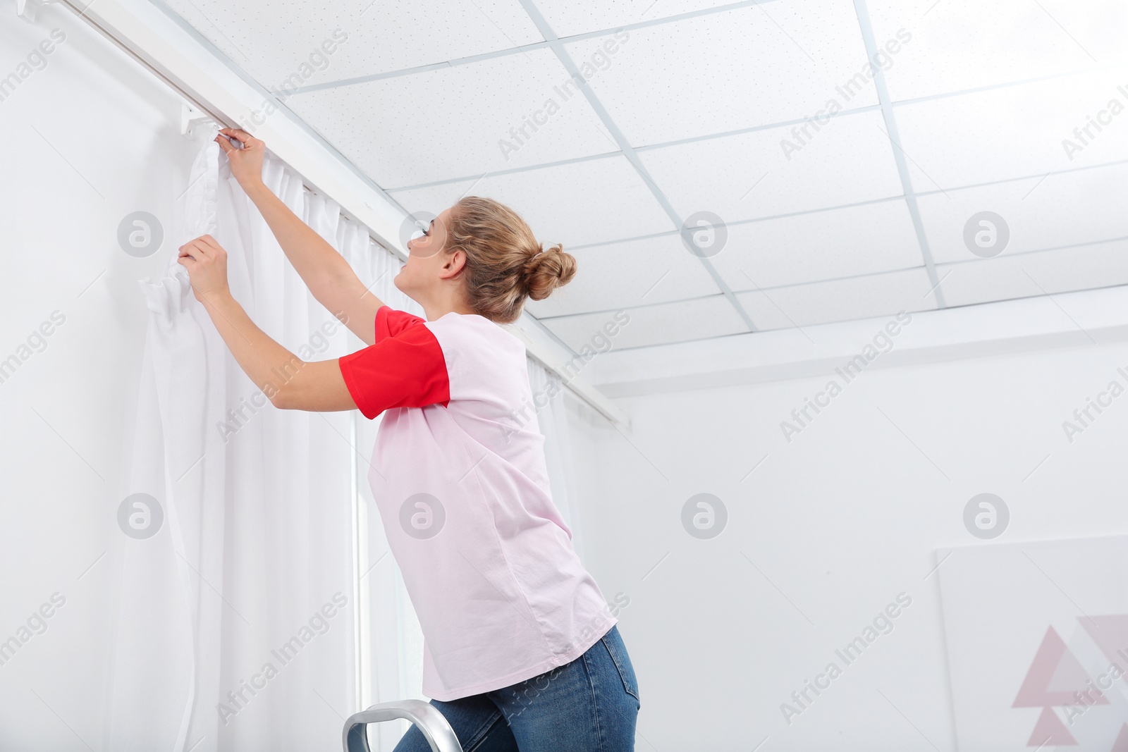 Photo of Woman hanging window curtain indoors. Interior decor element