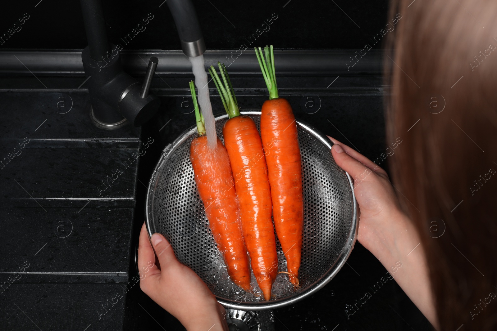 Photo of Woman washing fresh ripe juicy carrots under tap water in sink, above view