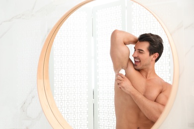 Photo of Handsome young man applying deodorant in bathroom. Space for text