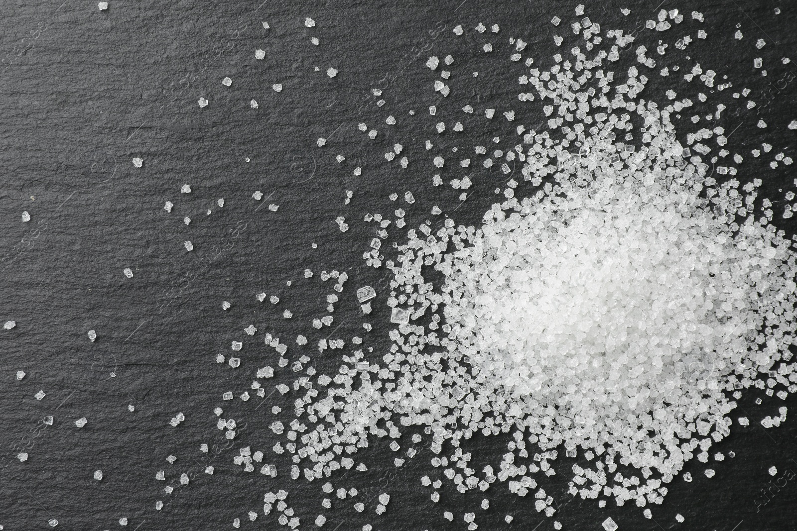 Photo of Heap of granulated sugar on black table, top view. Space for text