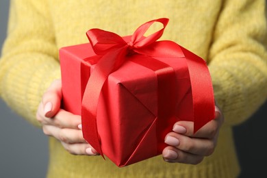 Photo of Christmas present. Woman holding gift box near grey wall, closeup