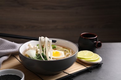 Photo of Eating delicious vegetarian ramen with chopsticks at grey table, space for text