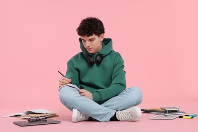 Portrait of student with notebook and stationery sitting on pink background