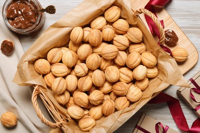 Photo of Wicker basket of delicious nut shaped cookies with boiled condensed milk on light wooden table, flat lay