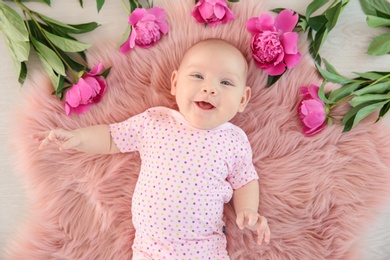 Photo of Adorable baby girl lying on fluffy rug with flowers, top view