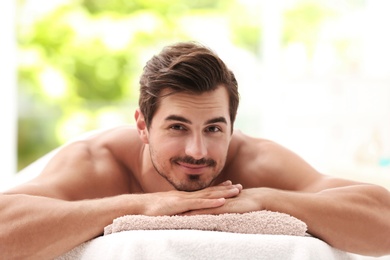 Handsome young man relaxing on massage table in spa salon