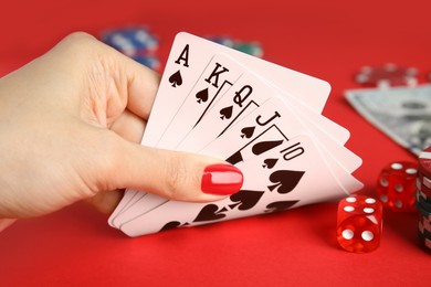 Photo of Woman holding playing cards with royal flush combination at red table, closeup