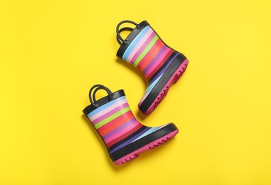 Photo of Pair of striped rubber boots on yellow background, top view