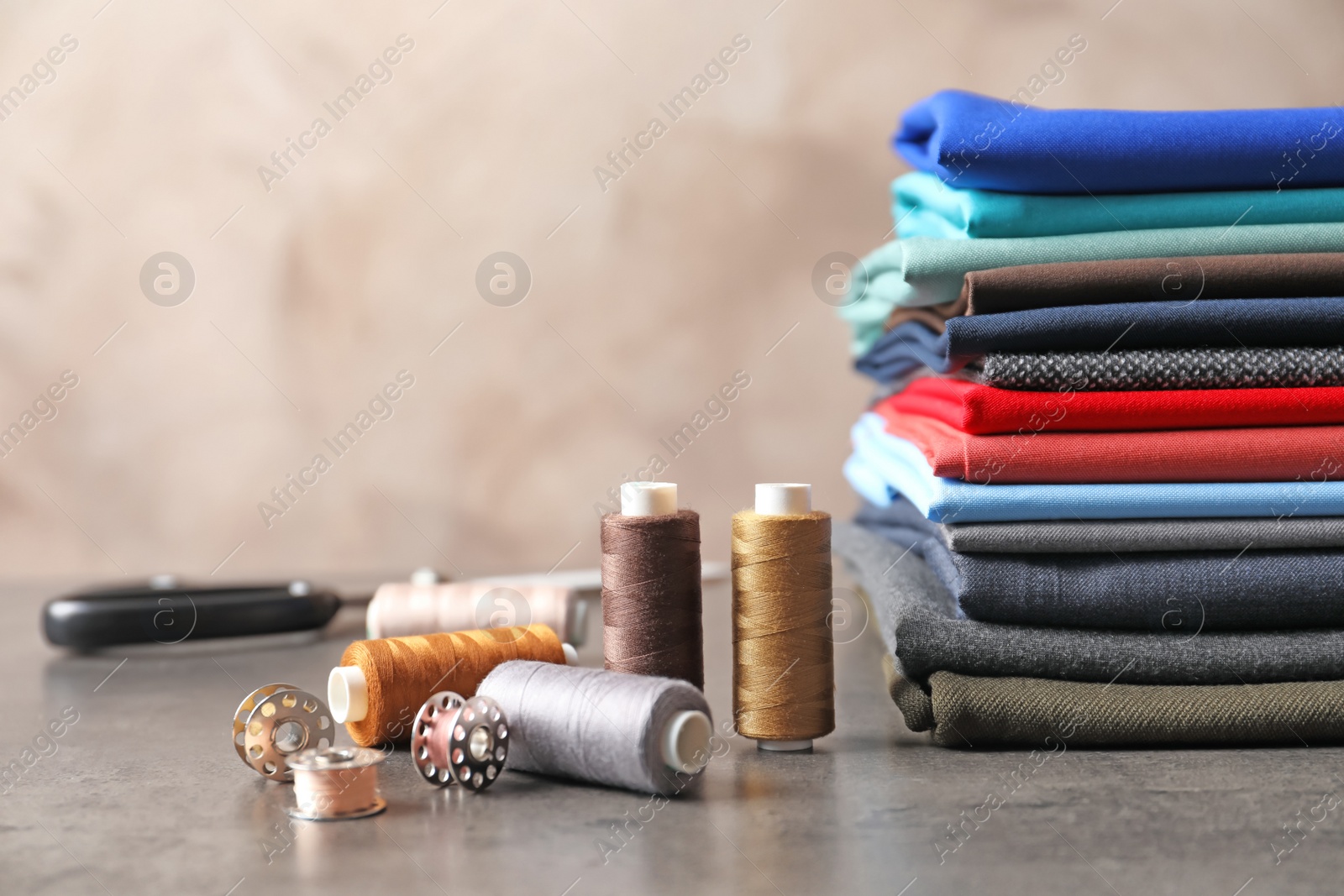 Photo of Bobbins with threads and stack of colorful fabrics on table. Tailoring accessories