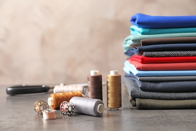 Bobbins with threads and stack of colorful fabrics on table. Tailoring accessories