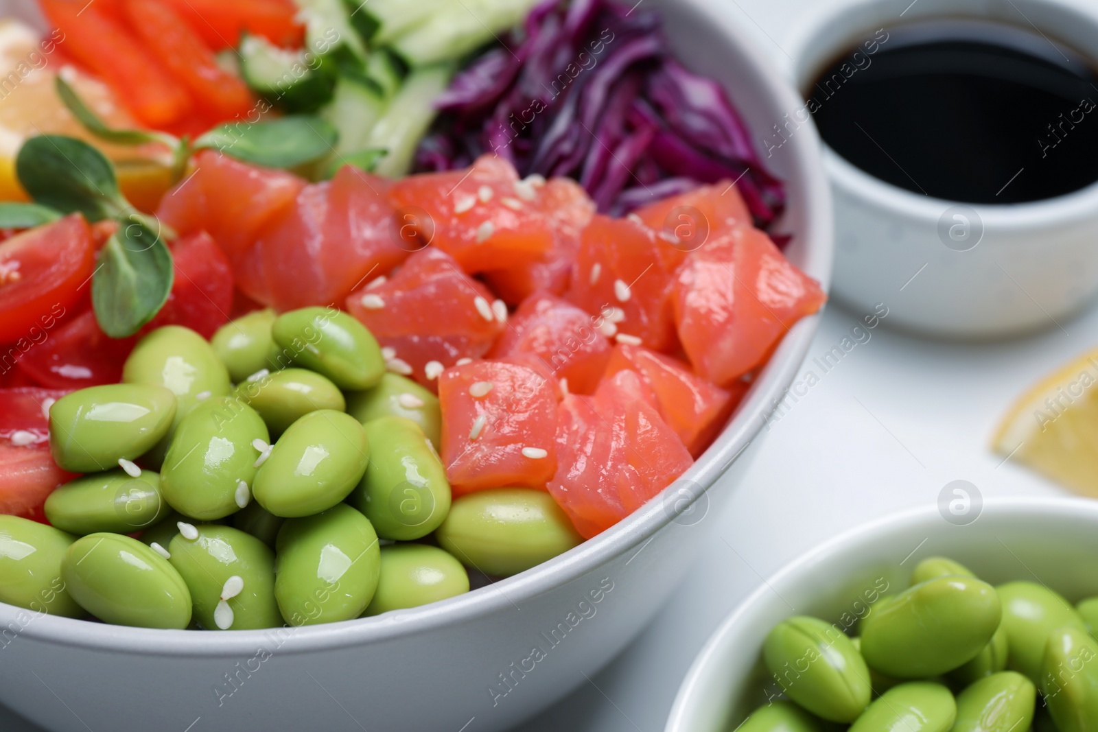 Photo of Poke bowl with salmon, edamame beans and vegetables on white table, closeup