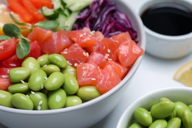 Photo of Poke bowl with salmon, edamame beans and vegetables on white table, closeup
