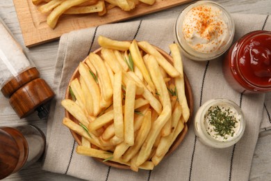 Delicious french fries served with sauces on light wooden table, flat lay