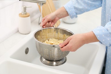 Photo of Woman rinsing pasta in colander above sink, closeup