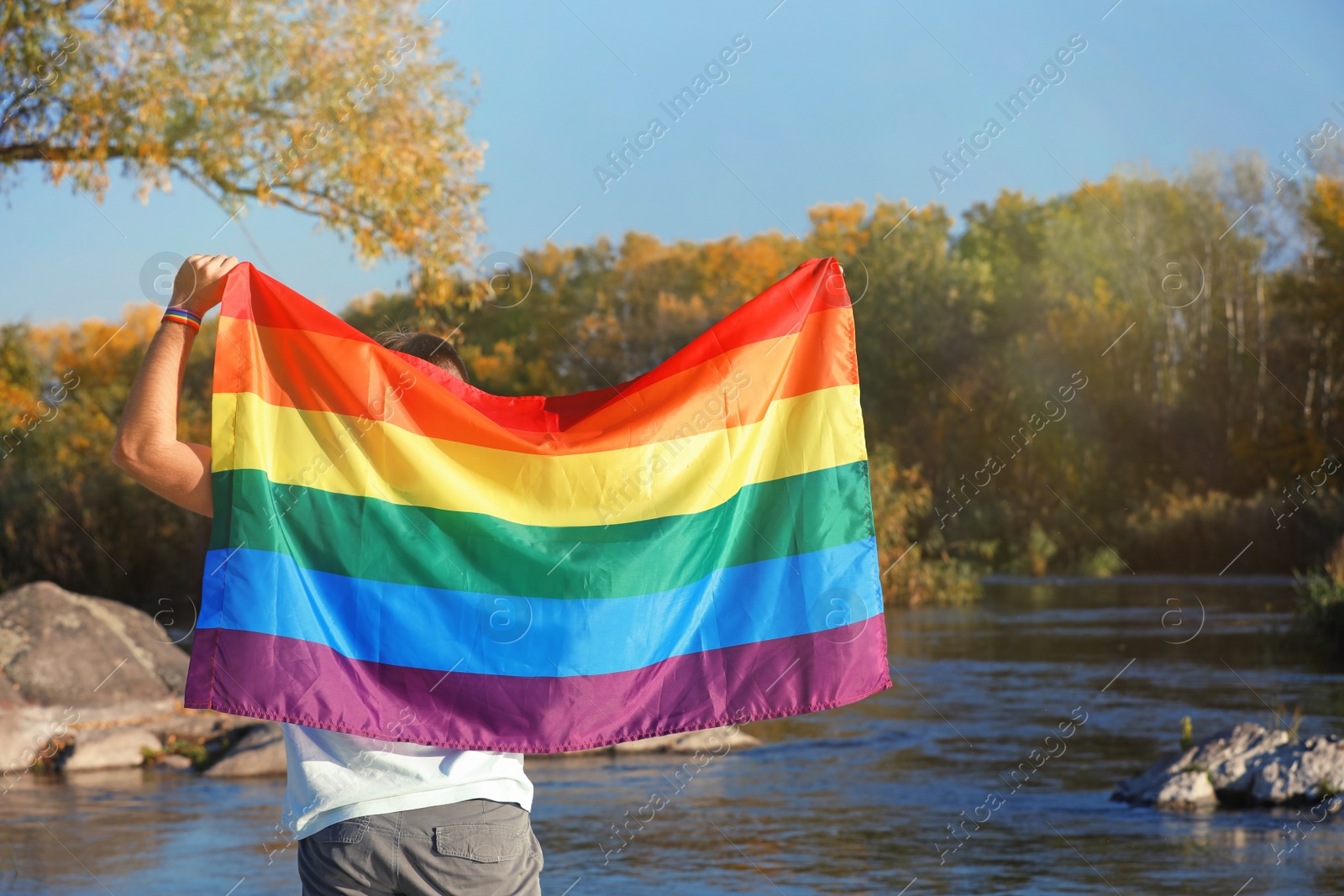 Photo of Man with rainbow LGBT flag outdoors, space for text. Gay symbol