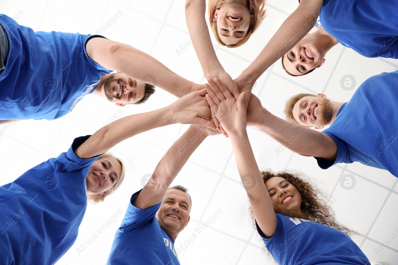 Photo of Team of volunteers putting their hands together on light background, bottom view