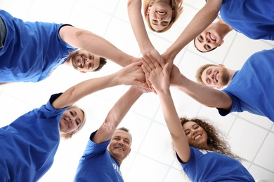 Photo of Team of volunteers putting their hands together on light background, bottom view