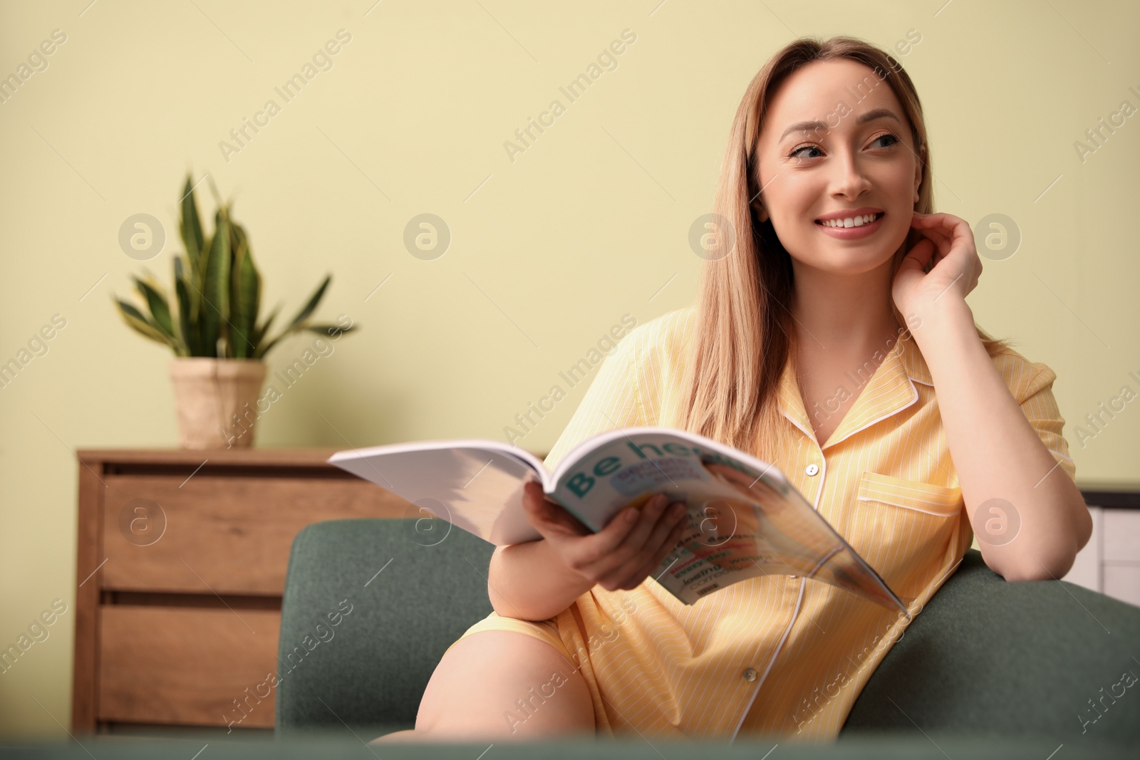 Photo of Happy woman reading magazine on sofa at home