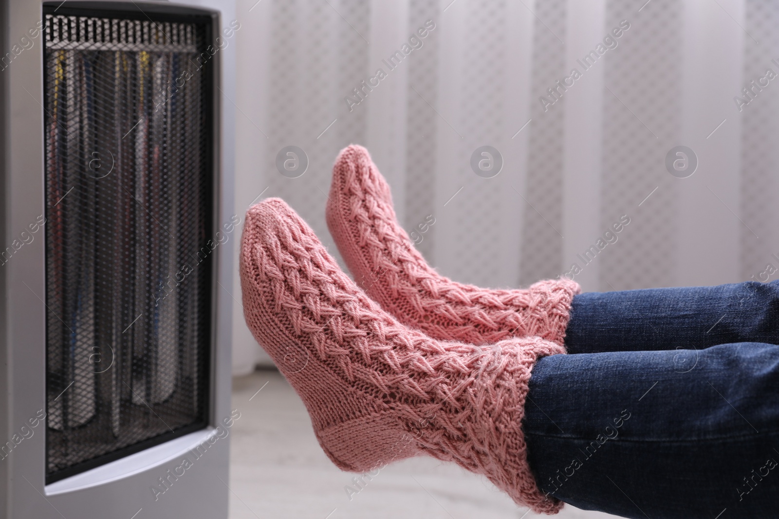 Photo of Woman warming feet near heater indoors, closeup