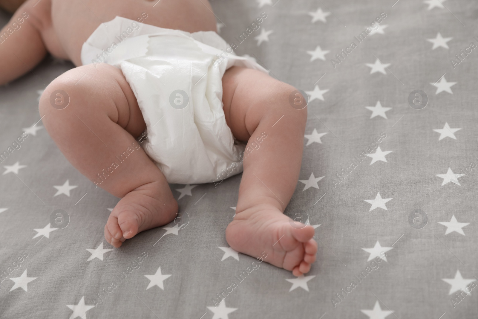 Photo of Cute little baby in diaper lying on bed, closeup