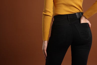 Photo of Woman wearing stylish black jeans on brown background, closeup. Space for text