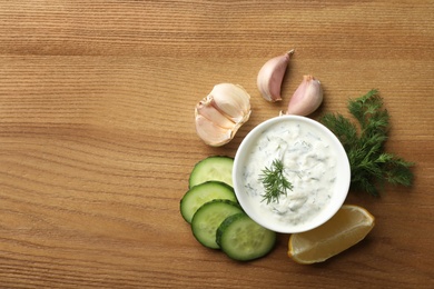 Photo of Cucumber sauce, ingredients and space for text on wooden background, flat lay. Traditional Tzatziki