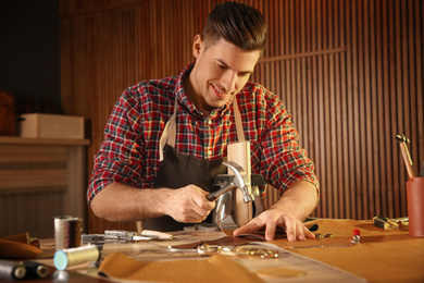 Photo of Man working with piece of leather at table in atelier