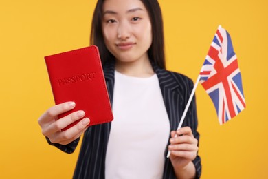 Immigration to United Kingdom. Woman with passport and flag on orange background, selective focus