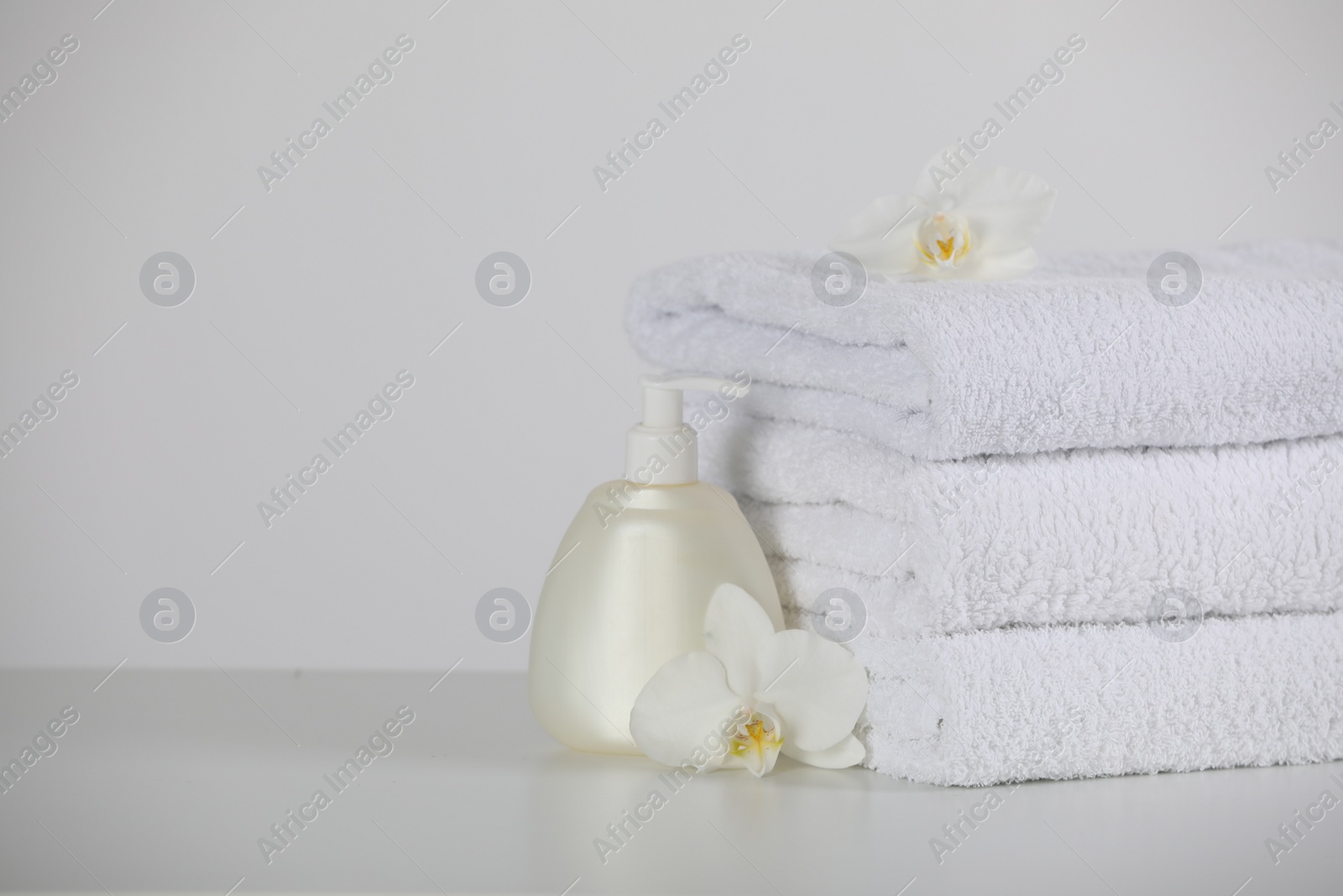 Photo of Soft folded towels, orchid flowers and dispenser on white table, space for text