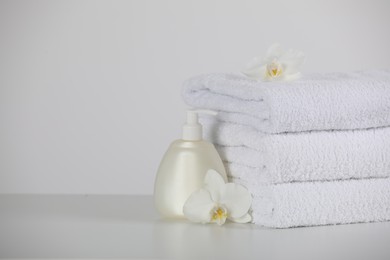 Soft folded towels, orchid flowers and dispenser on white table, space for text