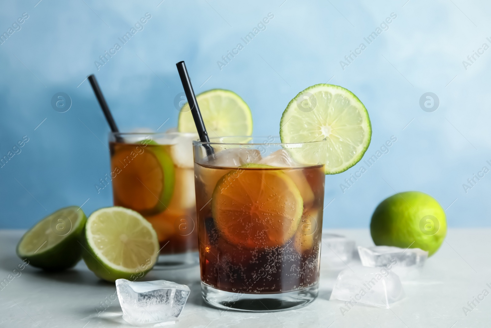 Photo of Glasses of cocktail with cola, ice and cut lime on table