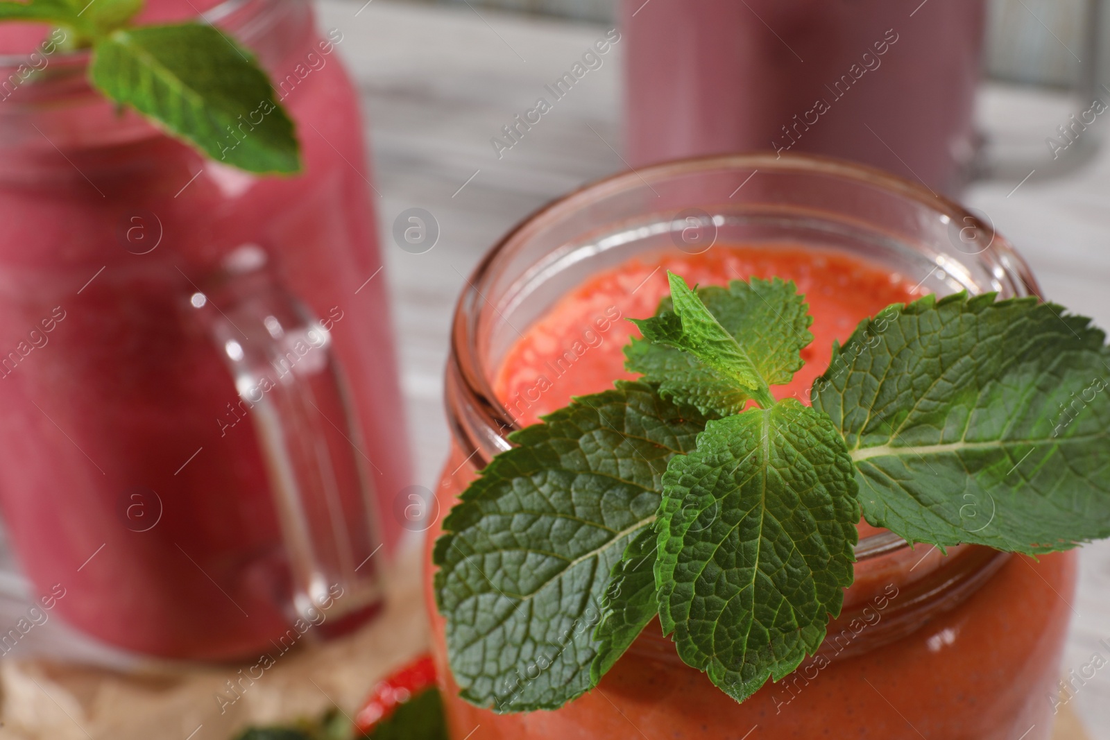 Photo of Mason jars of different tasty smoothies and mint on white wooden table, closeup