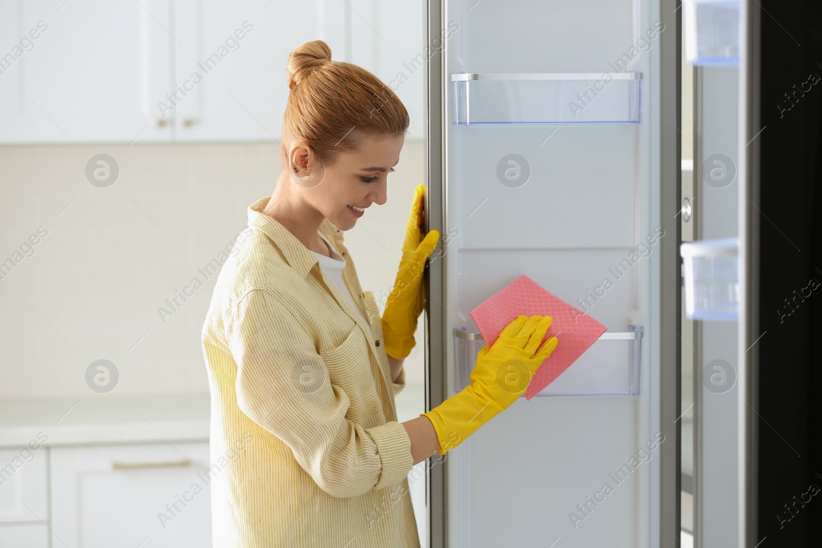 Photo of Woman in rubber gloves cleaning empty refrigerator at home