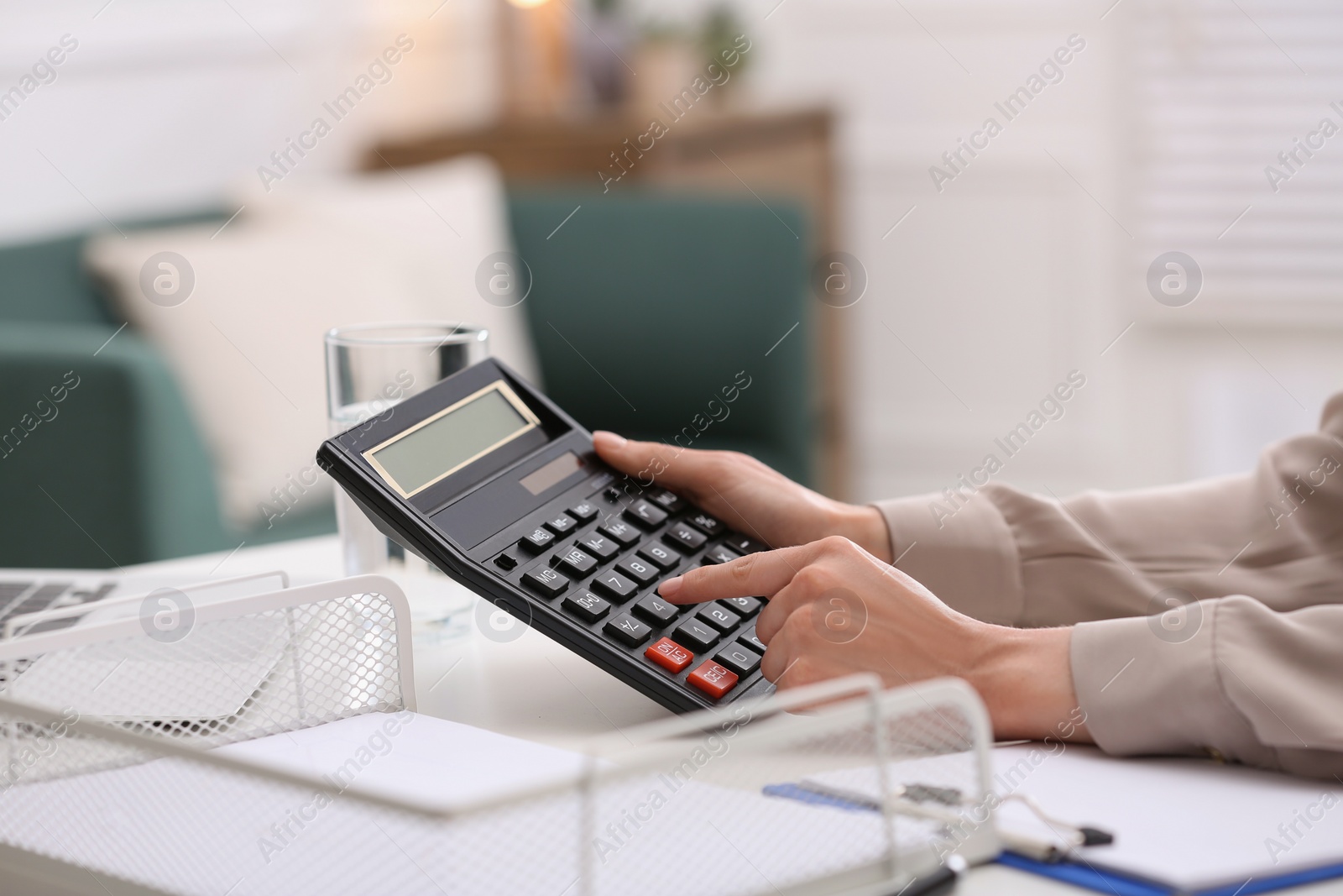 Photo of Woman using calculator at table indoors, closeup