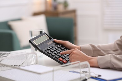 Photo of Woman using calculator at table indoors, closeup