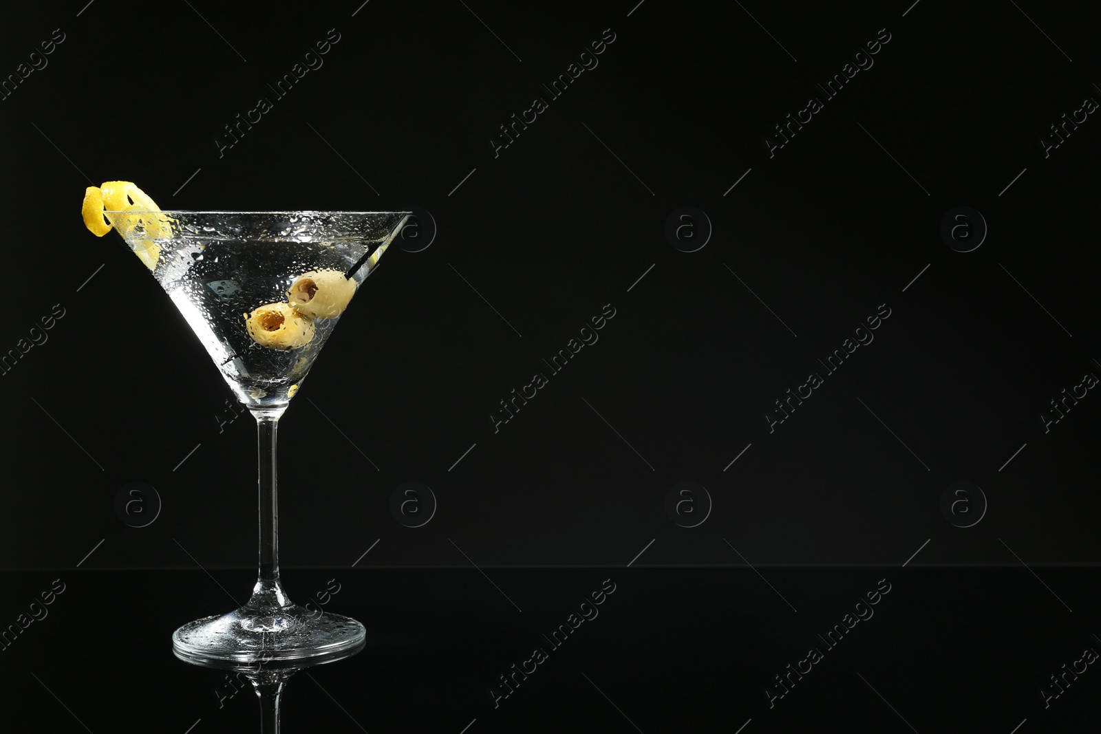 Photo of Martini cocktail with olives and lemon twist on dark background, space for text