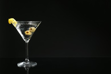 Photo of Martini cocktail with olives and lemon twist on dark background, space for text