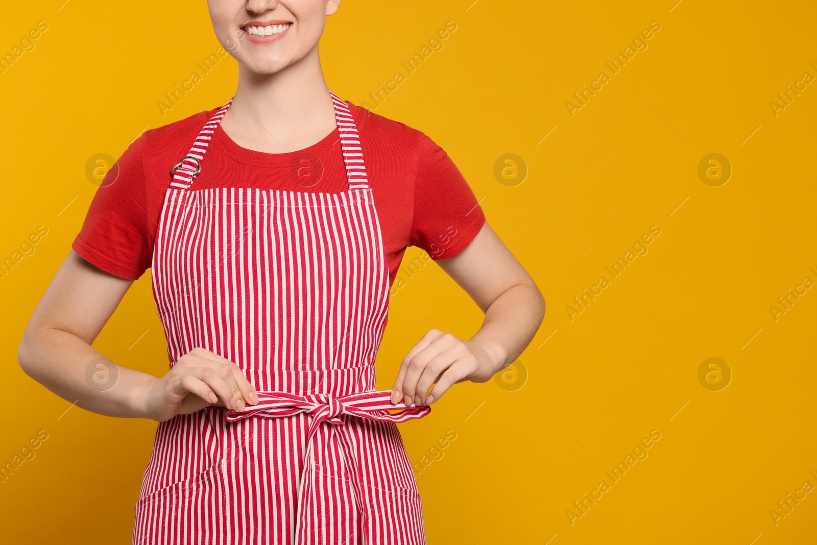 Photo of Woman in clean striped apron on orange background, closeup