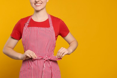 Photo of Woman in clean striped apron on orange background, closeup