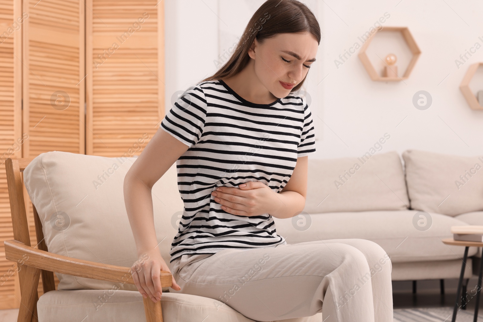 Photo of Young woman suffering from stomach pain at home