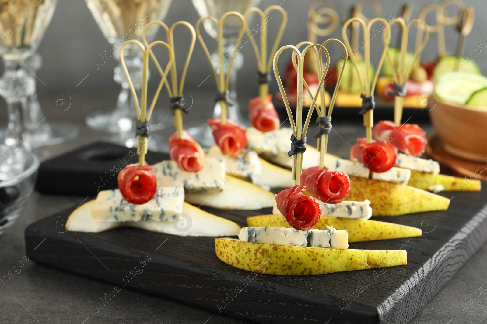 Photo of Tasty canapes with pears, blue cheese and prosciutto on grey table, closeup