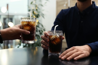 Photo of Couple with glasses of cold cola at table in cafe, closeup