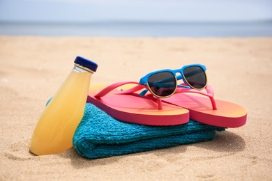 Photo of Stylish sunglasses, flip flops. towel and bottle of refreshing drink on beach, closeup