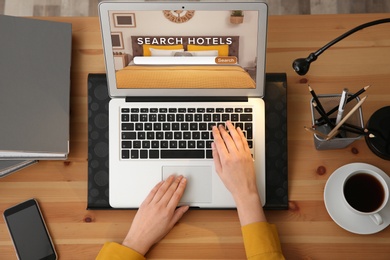 Woman searching hotel using laptop at table, top view. Booking online service